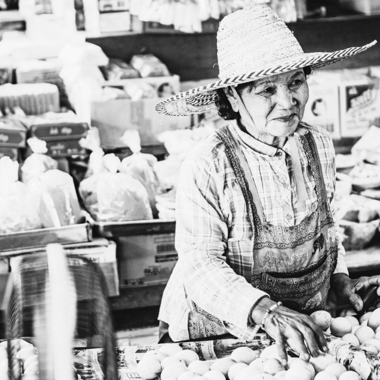 Vendeuse en chapeau, vendant des œufs dans un marché animé.