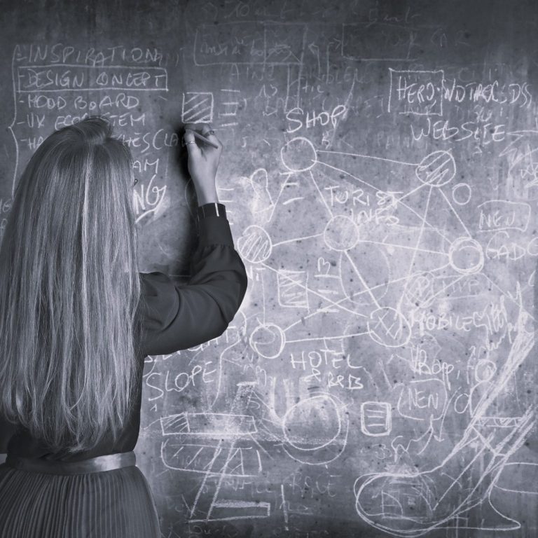 Femme écrivant des formules sur un tableau noir, entourée de diagrammes et de notes.